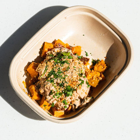 West African peanut stew with roasted sweet potatoes, peanut sauce, bell peppers, collard greens, tomatoes, crushed peanuts, and cilantro in bowl