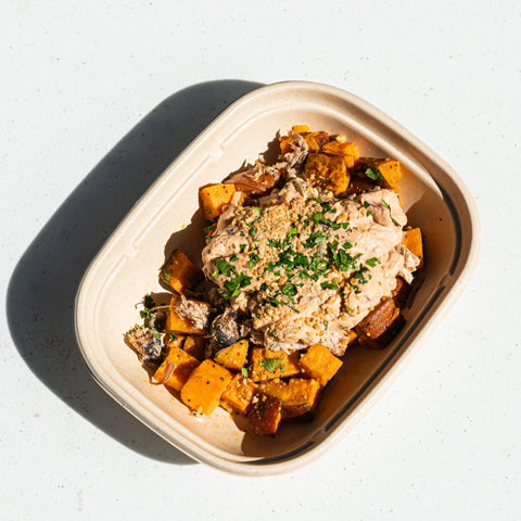 West African peanut stew with braised pork served with roasted sweet potatoes and garnished with crushed peanuts and cilantro in a tray